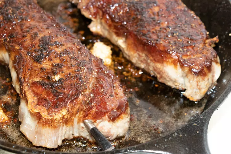 niman ranch new york strip steaks cooking in a cast iron skillet