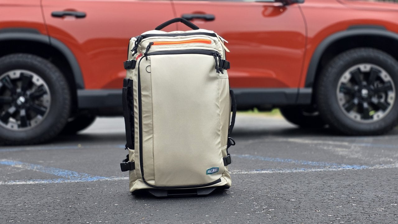 BagSmart Blast 43L Roller Backpack standing upright in a parking lot in front of an SUV