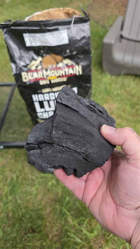 Hand holding a large chunk of Bear Mountain hardwood lump charcoal with the bag behind it