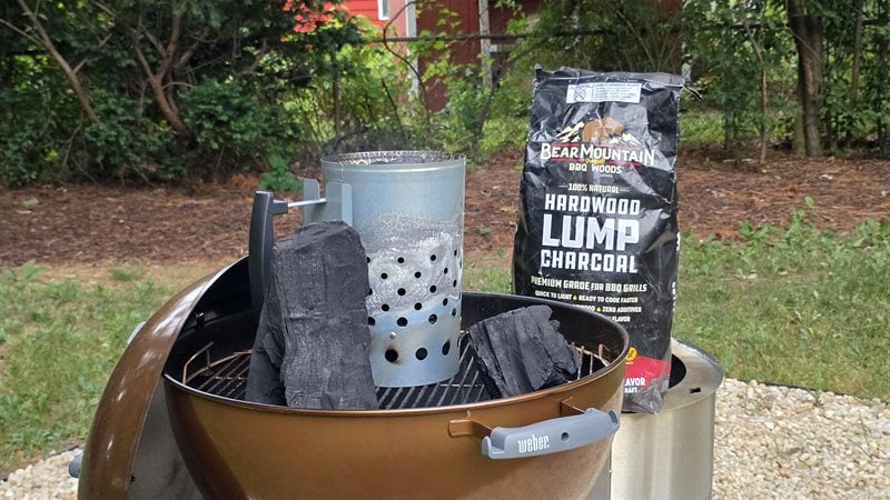 Chimney starter loaded with Bear Mountain hardwood lump charcoal on the Weber kettle grate beside the bag