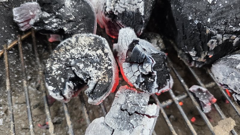 Bear Mountain lump charcoal glowing red under a coat of white ash on the Weber kettle grate