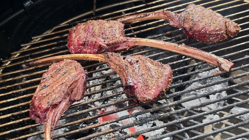 Four venison tomahawk chops searing over glowing lump charcoal on the Weber kettle grate