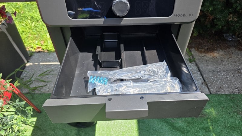 The built-in storage drawer on the Current Model G2 pulled open below the Model G2 badge, with the open bottom shelf of the cart visible underneath