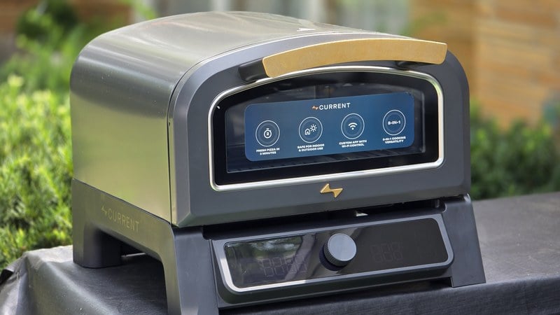 Current Model P+ smart electric pizza oven in slate on an outdoor cart, wooden handle and control dial visible