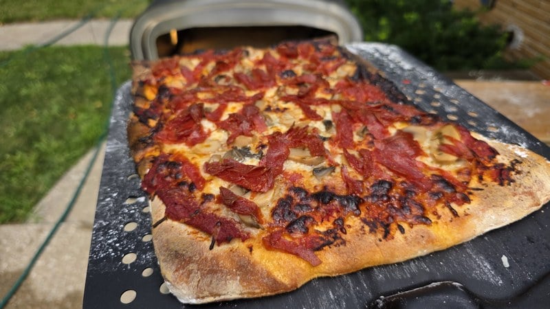 Windsor style pizza with shredded pepperoni and mushrooms, charred crust, resting on the Current perforated aluminum peel