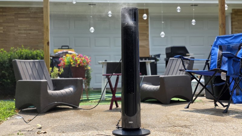 Dreo TurboCool 711AS misting on a concrete patio with lawn chairs and a grill in the background