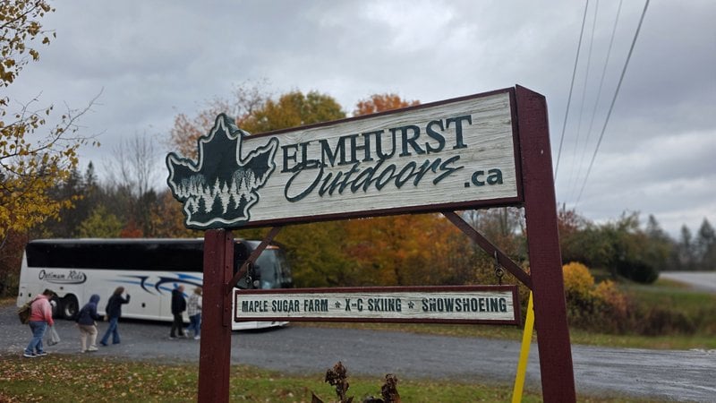 Elmhurst Outdoors sign listing maple sugar farm, cross-country skiing and snowshoeing, with a tour bus behind it