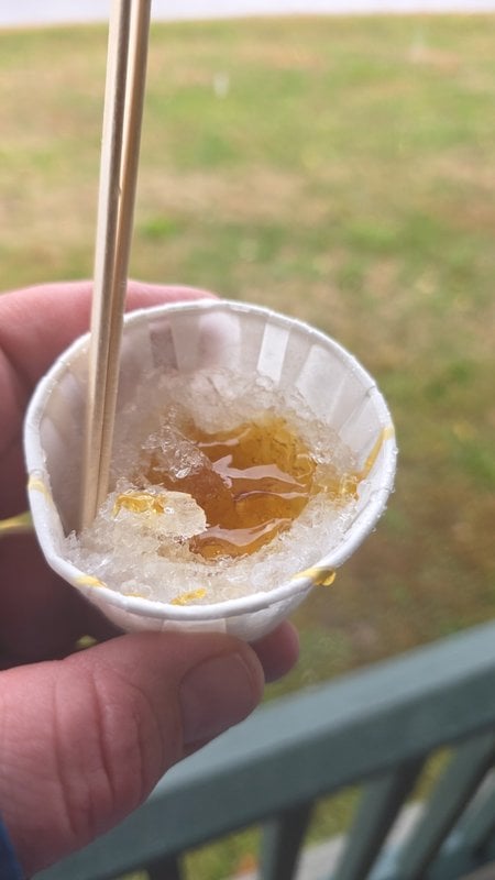 Maple taffy on snow, warm syrup poured over shaved ice in a paper cup with a wooden stick
