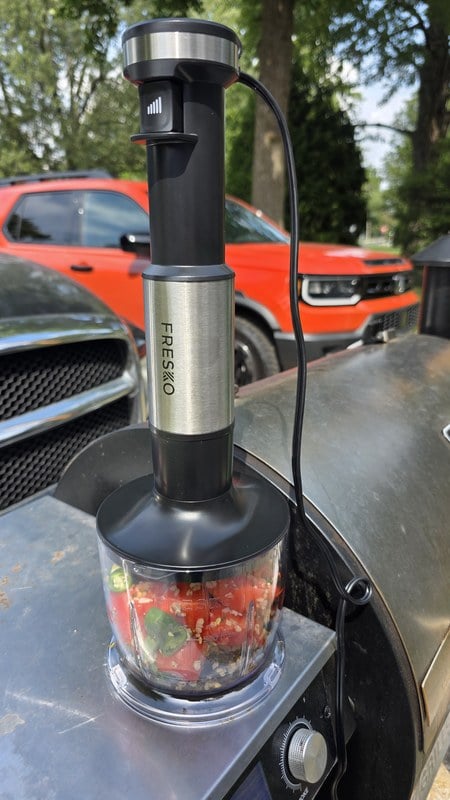 The FRESKO immersion blender standing in its chopper bowl full of fresh salsa on the side table of a grill outdoors