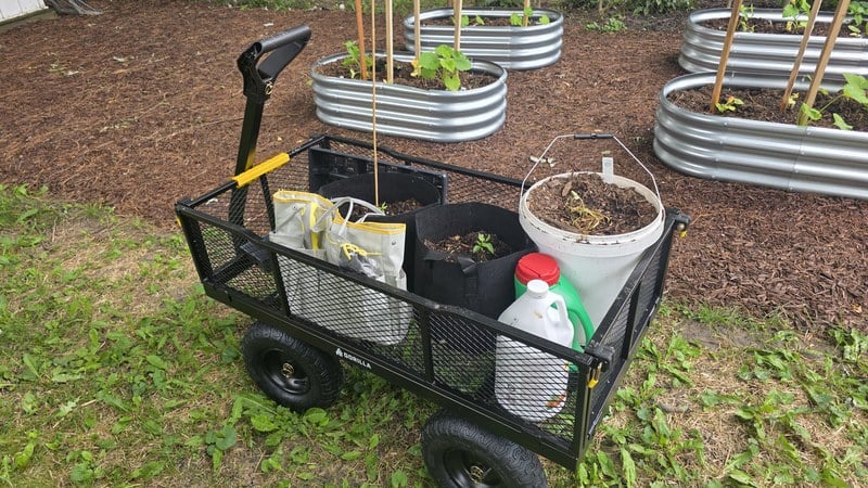 The Gorilla GCG-1200 loaded with buckets, grow bags, and a water jug in the garden
