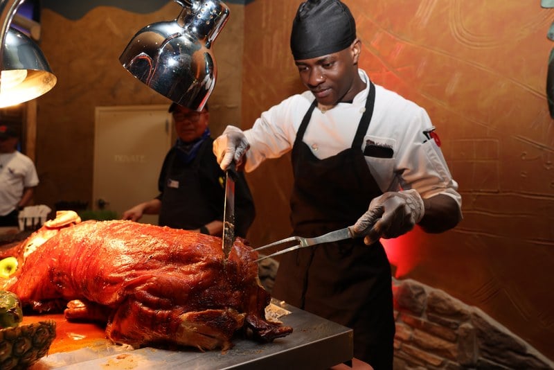 A Kalahari chef carving a whole roast pig at a festival carving station under heat lamps