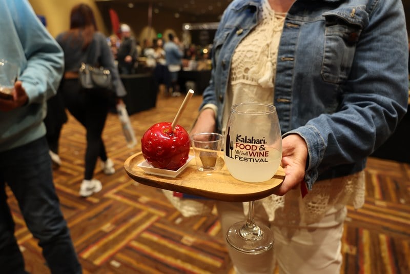 A guest holding the souvenir Kalahari Food and Not Just Wine Festival glass beside a candy apple dessert