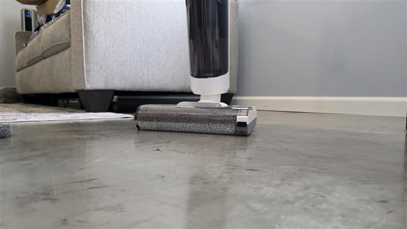 Kenmore AquaLite cleaning under couch edge showing baseboard reach on concrete floor
