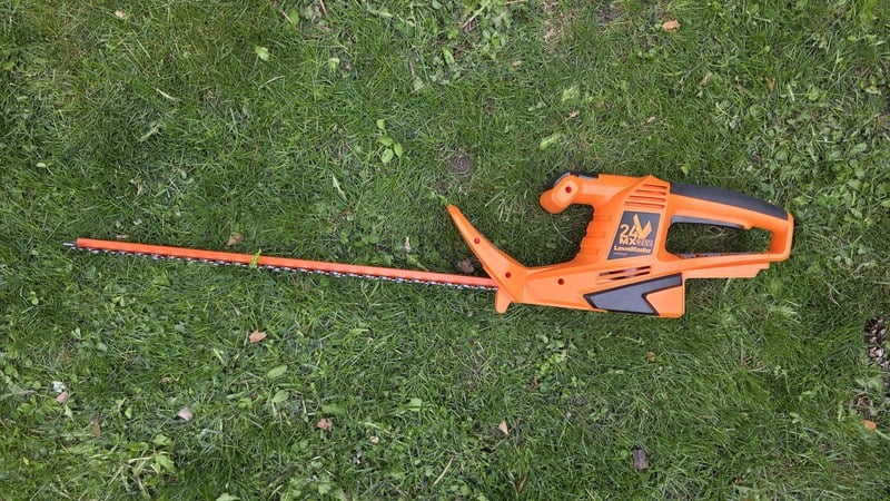 LawnMaster CLHT2422 22-inch cordless hedge trimmer with battery installed laying on freshly cut grass