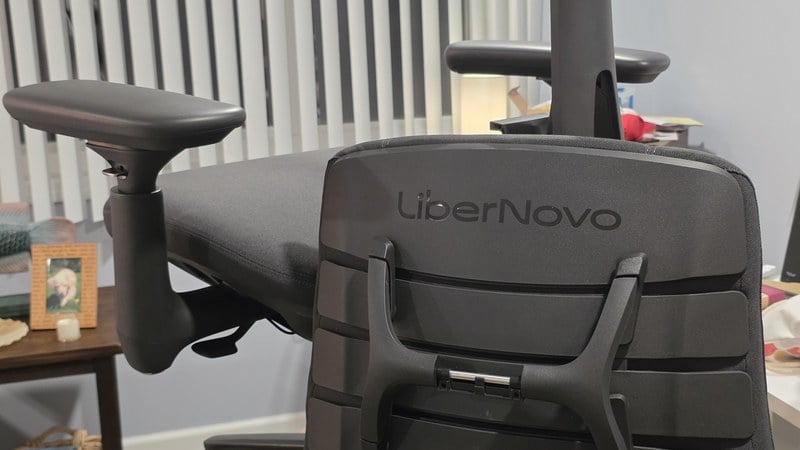 Close-up of a LiberNovo Maxis armrest and the back of the segmented backrest showing the LiberNovo logo and a mounting bracket
