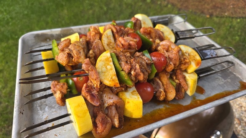 Raw marinated chicken kabobs with yellow squash, zucchini, green pepper and cherry tomatoes on flat metal skewers resting on a sheet pan
