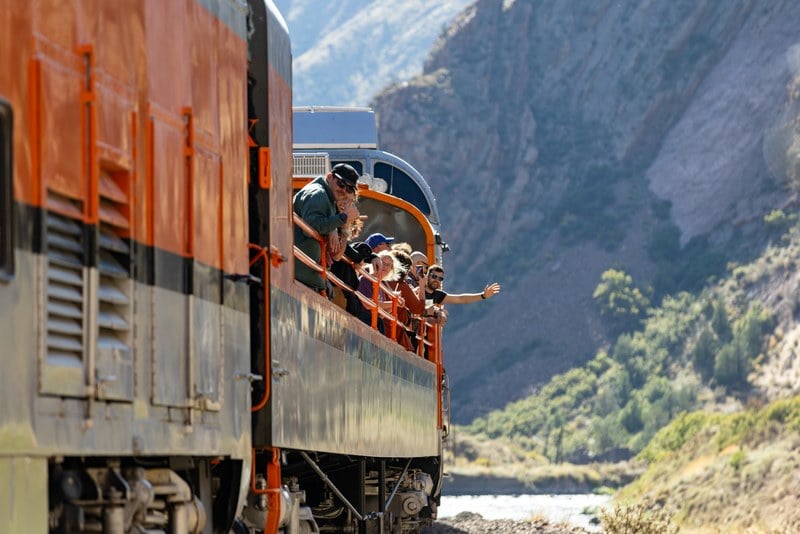 Passengers leaning over the rail of the Royal Gorge Route Railroad open-air car with the canyon behind them