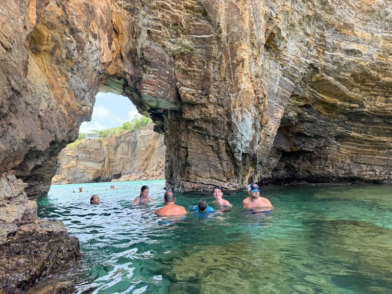 Charter guests swimming beneath a rock sea arch during a private boat day around St Martin