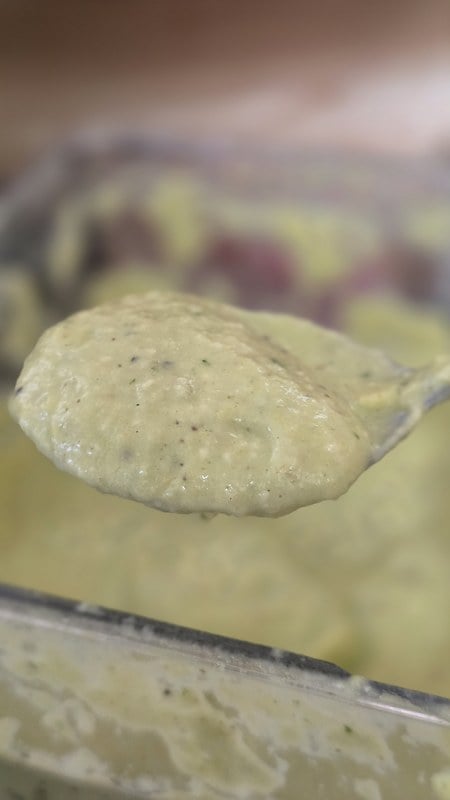 A spoonful of the finished summer squash sauce lifted from the blender, pale green and flecked with black pepper