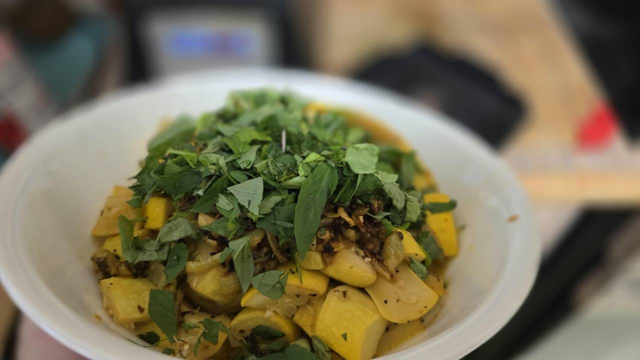 Cooked yellow summer squash and caramelized garlic in a white bowl under a heap of freshly picked basil