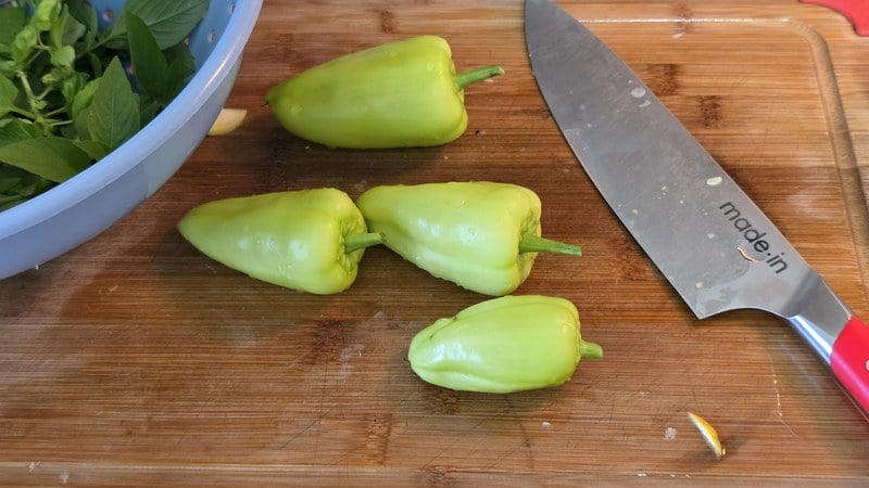 Four sweet Hungarian and Gypsy peppers from the garden on a cutting board beside a bowl of fresh basil