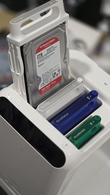 A Western Digital Red Plus drive lifted out of the UGREEN HomeAgent HA100 beside the Surveillance and Accelerator sleds