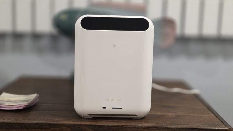 Front of the UGREEN HomeAgent HA100 with its top display panel, sitting on a wood dresser