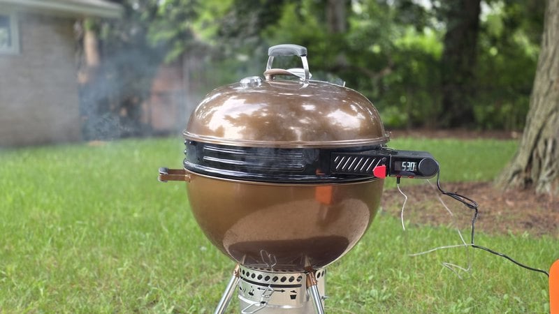 Weber Kettle Smart Ring installed between the bowl and lid of a copper Weber kettle with the LCD controller mounted on the side and smoke rising