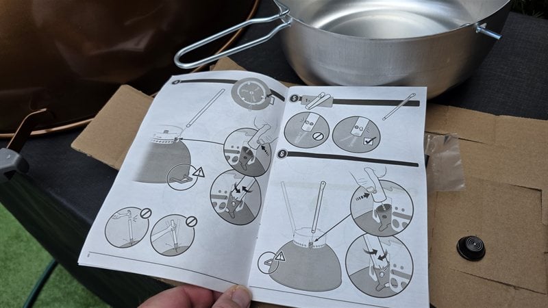 Weber Original Kettle Premium assembly instructions open on a table beside the ash catcher and grill parts