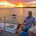 Three guys with drinks on a catamaran at sunset as dolphins surface on a Key West eco boat tour