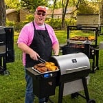 James Hills at the grill surrounded by a backyard cooking stack including a Masterbuilt Gravity Series smoker, a Z Grills pellet grill, a Santa Maria-style grill, and a stainless 4-burner gas grill