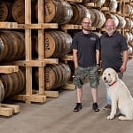 A father and son with their dog among the whiskey barrels in the rickhouse at Cedar Ridge Distillery in Iowa