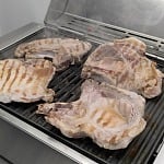 Four bone-in pork chops searing with grill marks on the Kenyon City Grill