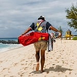 A golfer walks a Barbados beach carrying the red Mount Gay 1703 Devereux Golf bag and checkered towel