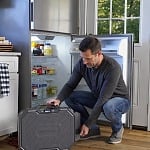 Man placing a 4Patriots portable power station next to an open refrigerator during a power outage