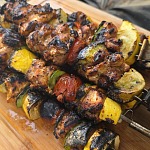 Grilled chicken kabobs with squash, zucchini, pepper and tomato, heavily charred, resting on a wooden cutting board