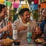 Three friends celebrating Cinco de Mayo with tequila, mezcal, and Fluere cocktails at an outdoor cantina under papel picado banners