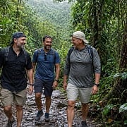 Three men hiking a wet rocky trail through the El Yunque rainforest in Puerto Rico