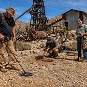 Three guys metal detecting and digging for treasure at an abandoned desert gold mine with a rusted headframe