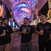 Three guys laughing on Fremont Street under the canopy holding drinks during a Vegas guys trip