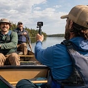 Three guys in a canoe on a northwoods lake, one filming the others with an action camera on a grip