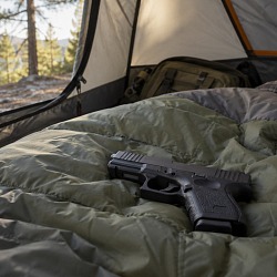 A handgun resting on a sleeping bag inside a tent at a lakeside campsite