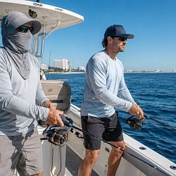Two men fishing off the coast of Alabama from a center console boat, one in a navy snapback and one in a sun-protection balaclava with wide brim