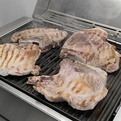 Four bone-in pork chops searing with grill marks on the Kenyon City Grill