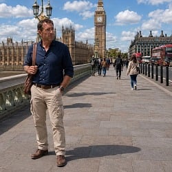 A man in well-fitted beige cargo pants and leather shoes walking across Westminster Bridge with Big Ben and the Houses of Parliament in the background