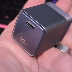 The UGREEN Nexode Air 65W GaN charger held in an open palm, its USB-C port and 65W label facing the camera