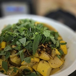 Cooked yellow summer squash and caramelized garlic in a white bowl under a heap of freshly picked basil