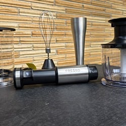 The FRESKO 4-in-1 immersion hand blender kit laid out on a table: measuring beaker with lid, whisk attachment, blending wand, motor body and the chopper bowl