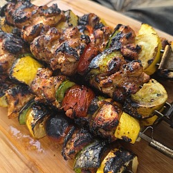 Grilled chicken kabobs with squash, zucchini, pepper and tomato, heavily charred, resting on a wooden cutting board