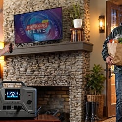 A 4Patriots portable power station running the TV during a storm outage as a man comes in from the rain with groceries and a jug of water